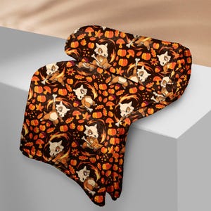 Op de afbeelding: Een donkerbruine deken met een herhalend patroon van oranje pompoenen, paddenstoelen en gestileerde Cubone-personages. De deken heeft een zachte, pluche uitstraling, met een gevouwen rand. Het ontwerp bevat herfstkleuren en thema's.