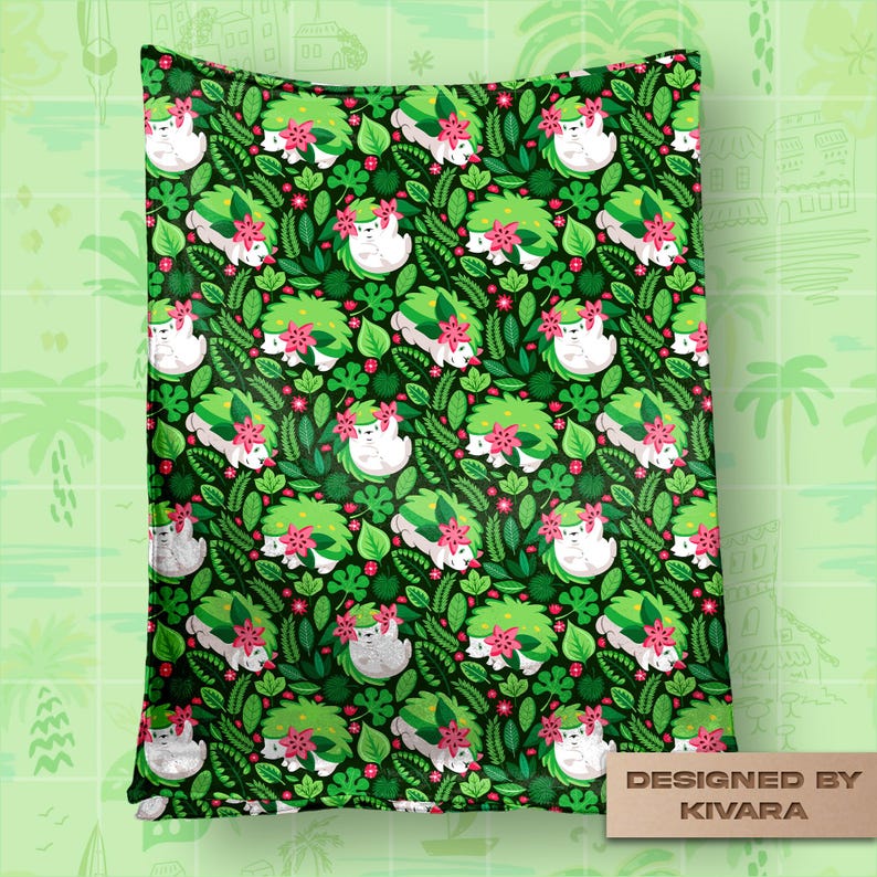 Op de afbeelding: Een groene deken met een herhalend patroon van witte, egelachtige wezens met groene en roze bloemaccenten, omringd door groene bladeren en rode bessen. De deken heeft een donkergroene achtergrond en de tekst "DESIGNED BY KIVARA".