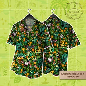 Pode incluir: Uma camisa de manga curta com botões, apresentando uma estampa completa de várias criaturas de desenho animado verdes e amarelas, intercaladas com flores laranja e folhagem verde sobre um fundo verde escuro, exibida em dois cabides pretos.