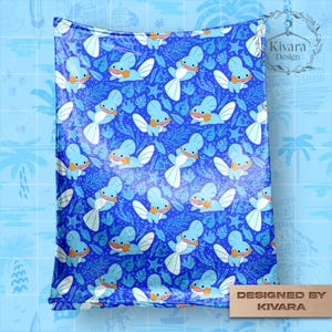 May include: A blue blanket with a repeating pattern of cartoon-style blue creatures with white wings and orange accents. The design includes starfish and leafy elements on a blue background. The blanket is labeled "DESIGNED BY KIVARA".