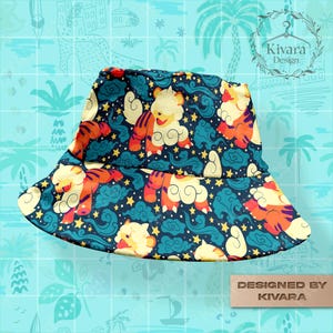 Peut inclure: Un chapeau bob bleu marine avec un motif répété de tigres de dessin animé, de nuages et d'étoiles. Les tigres sont orange et jaune, sur un fond de nuages turquoise et d'étoiles jaunes. Le chapeau est étiqueté "Designed by KIVARA."