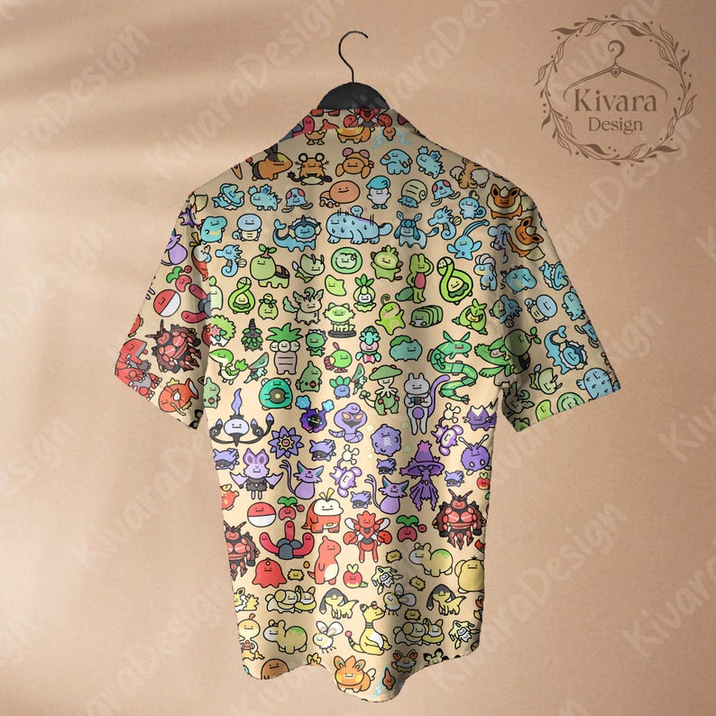 May include: A short-sleeved button-down shirt with a beige background and a colorful pattern of cartoon characters. The shirt is hanging on a black hanger. The shirt's design includes various creatures in shades of green, blue, red, and purple.