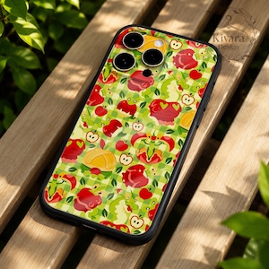 Puede incluir: Una funda para smartphone con un patrón repetitivo de manzanas rojas, hojas verdes e ilustraciones de pequeños dragones verdes sobre un fondo de cuadros verde claro y blanco. La funda tiene un borde negro y un recorte para triple cámara.