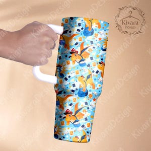 K&ouml;nnte beinhalten: Ein gro&szlig;er Becher mit wei&szlig;em Griff, verziert mit einem sich wiederholenden Muster von Zeichentrickdrachen mit H&uuml;ten und Overalls auf hellblauem Hintergrund mit Sternen und Spielkartensymbolen. Der Becher wird von einer Hand gehalten.