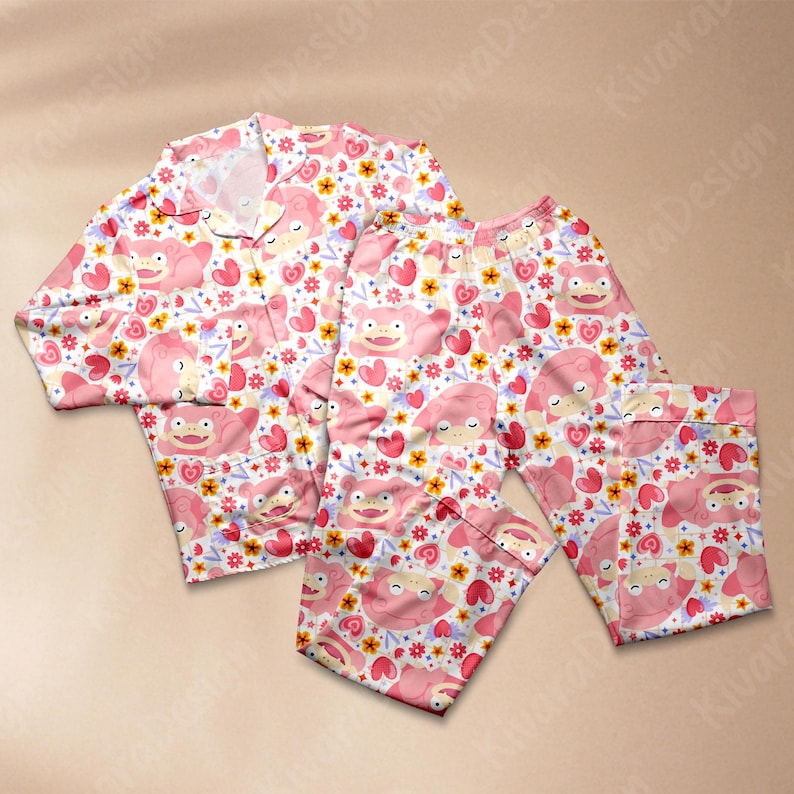K&ouml;nnte beinhalten: Rosa Pyjama-Set mit einem sich wiederholenden Muster aus Cartoon-Figuren, Herzen und Blumen auf wei&szlig;em Hintergrund. Das Set enth&auml;lt ein Hemd mit Kn&ouml;pfen und eine Hose mit elastischem Bund.