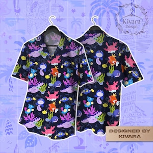 May include: Navy blue short-sleeve shirt with a colorful sea creature pattern. The design includes cartoon fish, crabs, and coral. The shirt is displayed on a black hanger. The text "DESIGNED BY KIVARA" is visible.