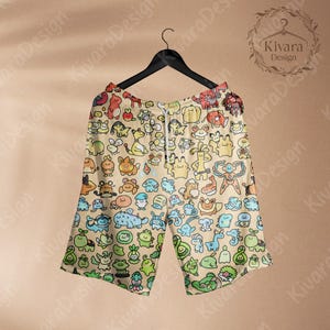 May include: Tan shorts with a repeating pattern of colorful cartoon characters. The shorts have a drawstring waist and are hanging on a black hanger. The shorts are a light tan color with a variety of cartoon characters in shades of blue, green, orange, and yellow.