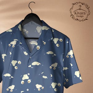 May include: A short-sleeved button-down shirt in dark blue featuring an all-over pattern of small, light-coloured, blob-like creatures. The shirt has a notched collar and is displayed on a black hanger. The logo Kivara Design is visible.
