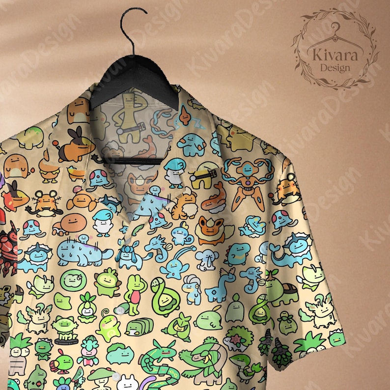 May include: A short-sleeved button-down shirt with a beige background and a colorful cartoon character pattern. The shirt is hanging on a black hanger. The shirt features a variety of creatures in shades of blue, green, orange, and yellow.