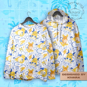 Puede incluir: Conjunto de sudadera y sudadera con capucha blancas con un patrón repetido de personajes de dibujos animados amarillos y naranjas, bombillas, rayos y baterías, con contornos azules. La sudadera con capucha tiene una capucha y el texto "Designed by KIVARA".