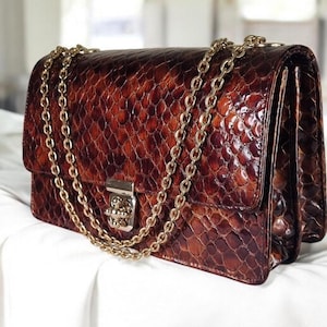 May include: A brown leather handbag with a gold chain strap and a textured snakeskin pattern.