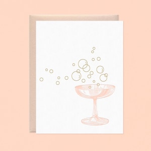 May include: A greeting card featuring a champagne glass with bubbles rising. The glass and bubbles are in a light pink color, with gold-colored outlines. The card is on a white background, with a light brown envelope.