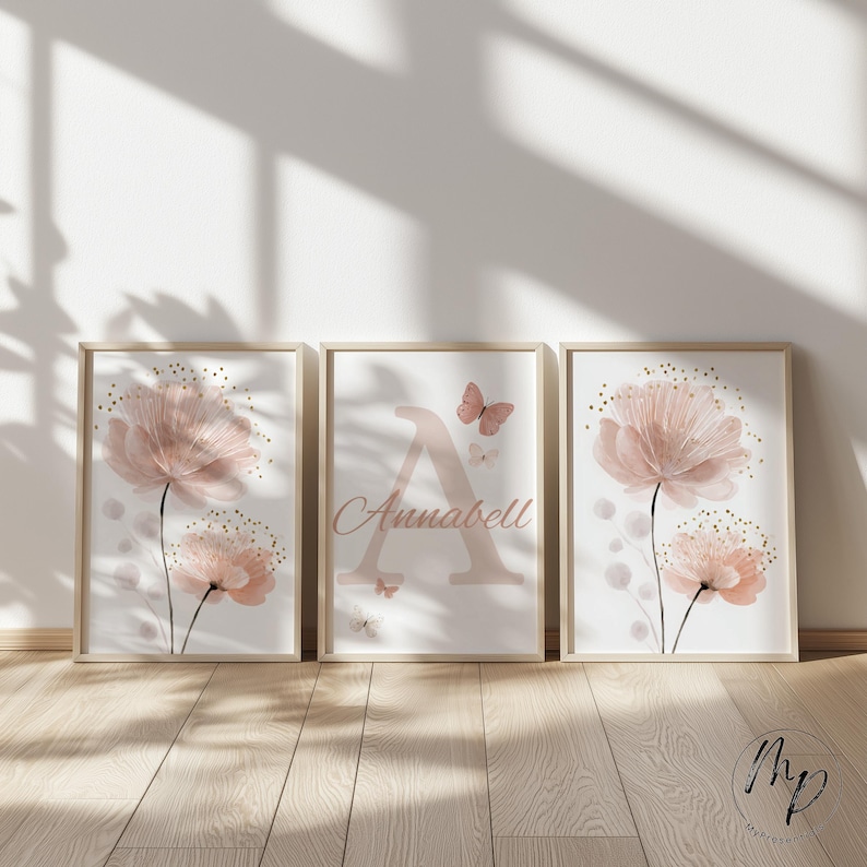 May include: Three framed floral art prints. The prints feature watercolor-style pink flowers with gold accents and a light pink background. The center print has the name "Annabell" and a letter "A". The frames are a light wood color.
