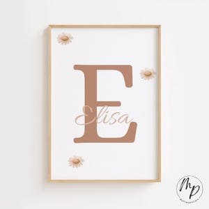 May include: A framed print featuring a large, brown letter "E" with the name "Elisa" in cursive script. The print is decorated with three daisy illustrations and has a light wood frame. The background is white.
