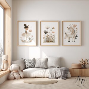 Puede incluir: Tres impresiones enmarcadas con marcos de madera clara. Las impresiones presentan una bailarina, un arreglo floral y un unicornio. La habitaci&oacute;n tiene una paleta de colores neutros con un sof&aacute; blanco, almohadas y una mesa auxiliar de madera. Un oso de peluche y un perro de peluche est&aacute;n en el alf&eacute;izar de la ventana.