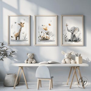 K&ouml;nnte beinhalten: Drei gerahmte Aquarelldrucke mit einer Giraffe, einem Blumenarrangement und einem Elefanten. Die Drucke haben helle Holzrahmen und weiche, neutrale Farben. Die Giraffe und der Elefant sind in einem skurrilen Stil gehalten, der f&uuml;r ein Kinderzimmer geeignet ist.