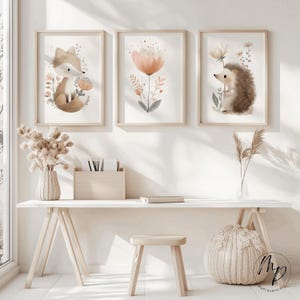 Puede incluir: Tres impresiones enmarcadas en acuarela con animales del bosque y flores. Las impresiones incluyen un zorro, una flor y un erizo. Los marcos son de madera clara y la obra de arte tiene una paleta de colores pastel. Las impresiones se exhiben en un escritorio blanco.