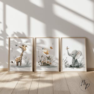 K&ouml;nnte beinhalten: Drei gerahmte Aquarelldrucke mit einer Giraffe, Schmetterlingen und einem Elefanten. Die Giraffe hat braune Flecken, die Schmetterlinge sind orange und grau, und der Elefant ist grau. Die Bilder sind in hellbraunen Rahmen gefasst.