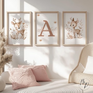 May include: Three framed art prints featuring a woodland theme. The prints include a deer illustration, a large letter "A" with the name "Annabel", and another deer illustration. The frames are light wood, and the artwork has a soft, neutral color palette.