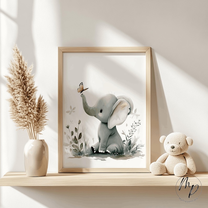 K&ouml;nnte beinhalten: Ein gerahmter Aquarelldruck eines grauen Babyelefanten mit einem Schmetterling auf seinem R&uuml;ssel. Der Elefant sitzt in einem Feld aus gr&uuml;nen und grauen Pflanzen. Der Druck ist in einem hellen Holzrahmen. Ein beiger Teddyb&auml;r sitzt auf einem Regal.