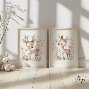 May include: Two framed art prints featuring watercolor illustrations of deer. The deer are depicted in a soft, neutral color palette with floral and botanical elements. The frames are light wood, adding a natural touch to the artwork.