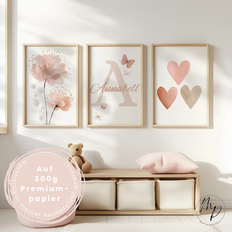 May include: Three framed art prints with a floral design, the letter "A" with the name "Annabell", and three hearts in shades of pink and beige. The prints are displayed above a wooden bench with storage cubes. A teddy bear and a pink pillow are also visible.