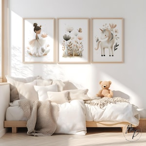 Puede incluir: Tres impresiones en acuarela enmarcadas que representan una bailarina, flores y un unicornio. Las impresiones est&aacute;n en marcos de madera clara sobre una cama con ropa de cama blanca, almohadas y un oso de peluche. La habitaci&oacute;n est&aacute; decorada en tonos neutros.