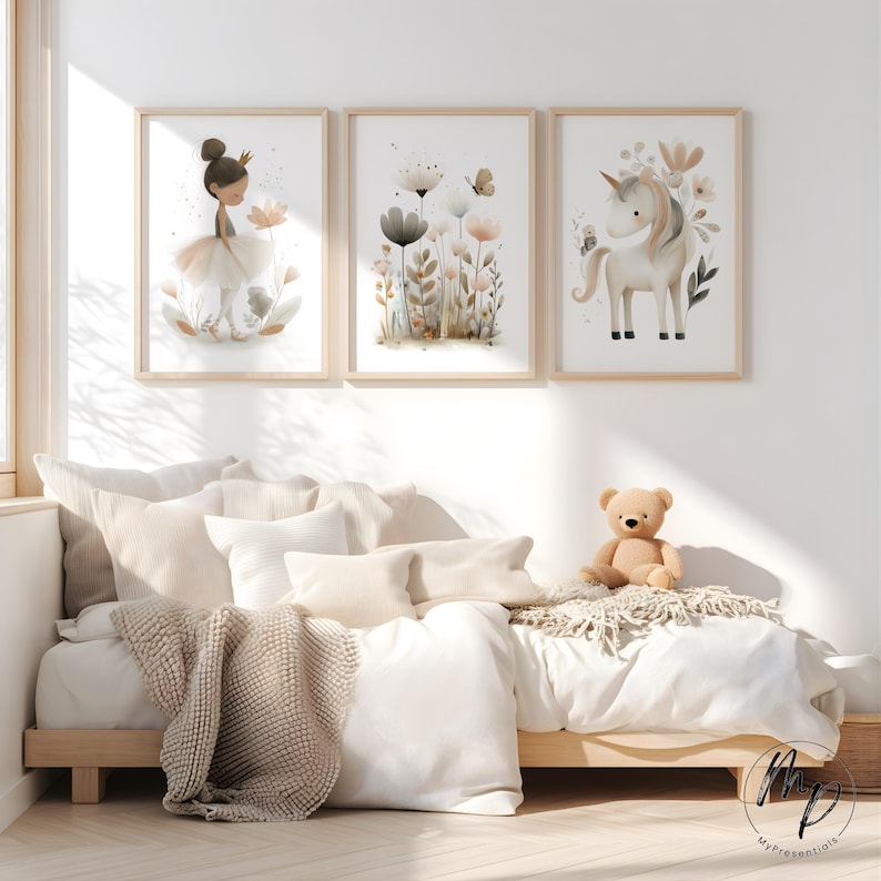 Puede incluir: Tres impresiones en acuarela enmarcadas que representan una bailarina, flores y un unicornio. Las impresiones est&aacute;n en marcos de madera clara sobre una cama con ropa de cama blanca, almohadas y un oso de peluche. La habitaci&oacute;n est&aacute; decorada en tonos neutros.