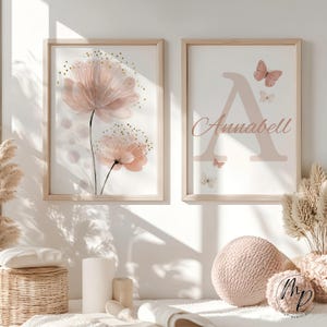 May include: Two framed art prints. One features a watercolor floral design in shades of pink and gold. The other displays the letter "A" with the name "Annabell" and butterfly illustrations in pink. Both are in light wood frames.