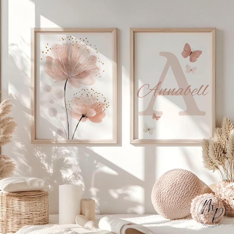 May include: Two framed art prints. One features a watercolor floral design in shades of pink and gold. The other displays the letter "A" with the name "Annabell" and butterfly illustrations in pink. Both are in light wood frames.