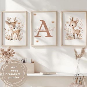May include: Three framed art prints featuring a fawn, a large letter "A" with the name "Annabel", and another fawn. The artwork has a soft, neutral color palette with floral and botanical elements. The frames are light wood.
