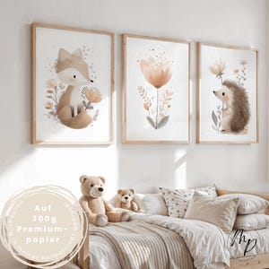 Puede incluir: Tres impresiones enmarcadas en acuarela con animales del bosque y flores. Las impresiones incluyen un zorro, una flor y un erizo. Los marcos son de madera clara. Las impresiones se exhiben sobre una cama con osos de peluche y almohadas.