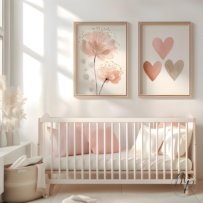 May include: Two framed wall art prints featuring watercolor floral and heart designs in soft pink and neutral tones. A white crib with pink pillows and a neutral basket with linens complete the nursery decor.