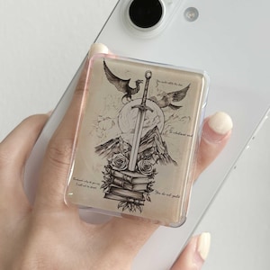 Op de afbeelding: Een doorzichtige telefoonhouder met een fantasieontwerp. De zwart-wit illustratie toont een zwaard, vogels, bergen, boeken en rozen. De houder heeft de tekst "You do not yield."