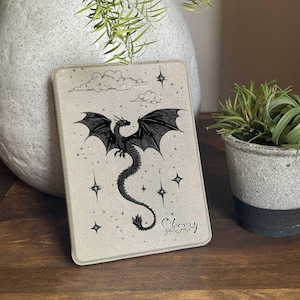 May include: A beige Kindle cover featuring a black dragon flying in front of a white cloud and stars. The name "Sherry" is written in cursive at the bottom.