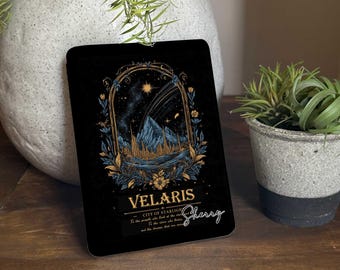 May include: Black rectangular item with a celestial design featuring the text "VELARIS CITY OF STARLIGHT". The artwork includes a mountain range, stars, and floral accents in gold and blue. A signature reads "Sherry".