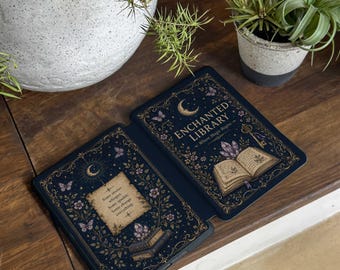 May include: A dark blue e-reader cover featuring a gold crescent moon, butterflies, and floral motifs. The right side displays an open book with the text ENCHANTED LIBRARY Where Magic Begins. The left side shows a parchment with the text Some stories whisper. Some sparkle. Some change everything.