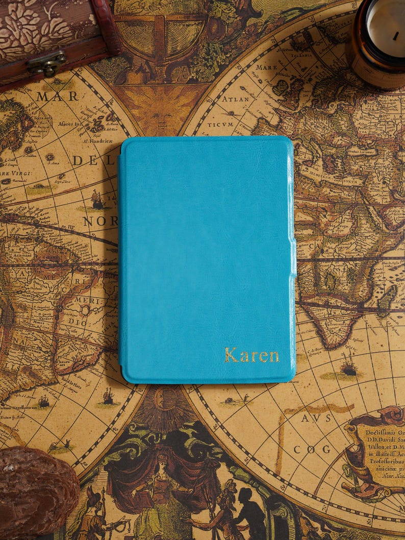 May include: A turquoise leather-bound journal with the name "Karen" in gold lettering. The journal is set on a vintage world map, with a small wooden chest in the background. The journal is rectangular and appears to be closed.