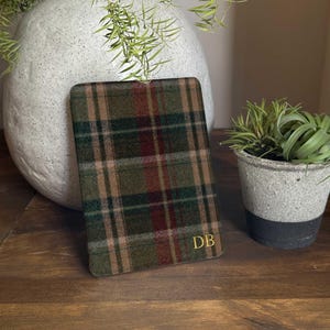 May include: A rectangular e-reader or tablet sleeve featuring a green, brown, and red plaid pattern. The bottom right corner of the sleeve is personalised with the gold-coloured embossed initials DB in a classic serif font style.