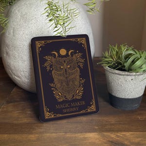 Op de afbeelding: Een rechthoekige zwarte plaquette met een goudkleurige lijntekening van een uil omringd door bladeren en maanfasen. De tekst MAGIC MAKER SHERRY staat in goud onderaan gedrukt, omlijst door een sierlijke gouden rand op het vooroppervlak.