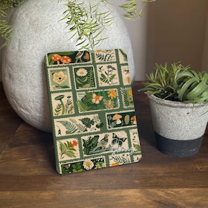 Könnte beinhalten: Ein grünes Notizbuch mit einer Collage aus Vintage-Briefmarken, die Naturmotive zeigen, darunter Pilze, Schmetterlinge, Vögel und Blumen. Der Text "Cherry" steht in der rechten unteren Ecke des Notizbuchs.