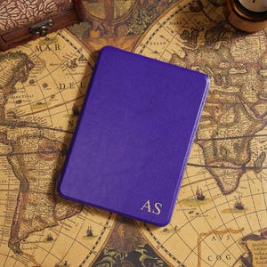 May include: A purple leather-bound journal with the gold initials "AS" on the cover. The journal is rectangular and sits on a vintage map. A small wooden box and a candle are also visible.