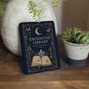 May include: A rectangular sign with a dark blue background featuring gold filigree borders, a crescent moon, butterflies, a key, purple crystals, and an open book. The text reads ENCHANTED LIBRARY and Where Magic Begins in gold lettering.
