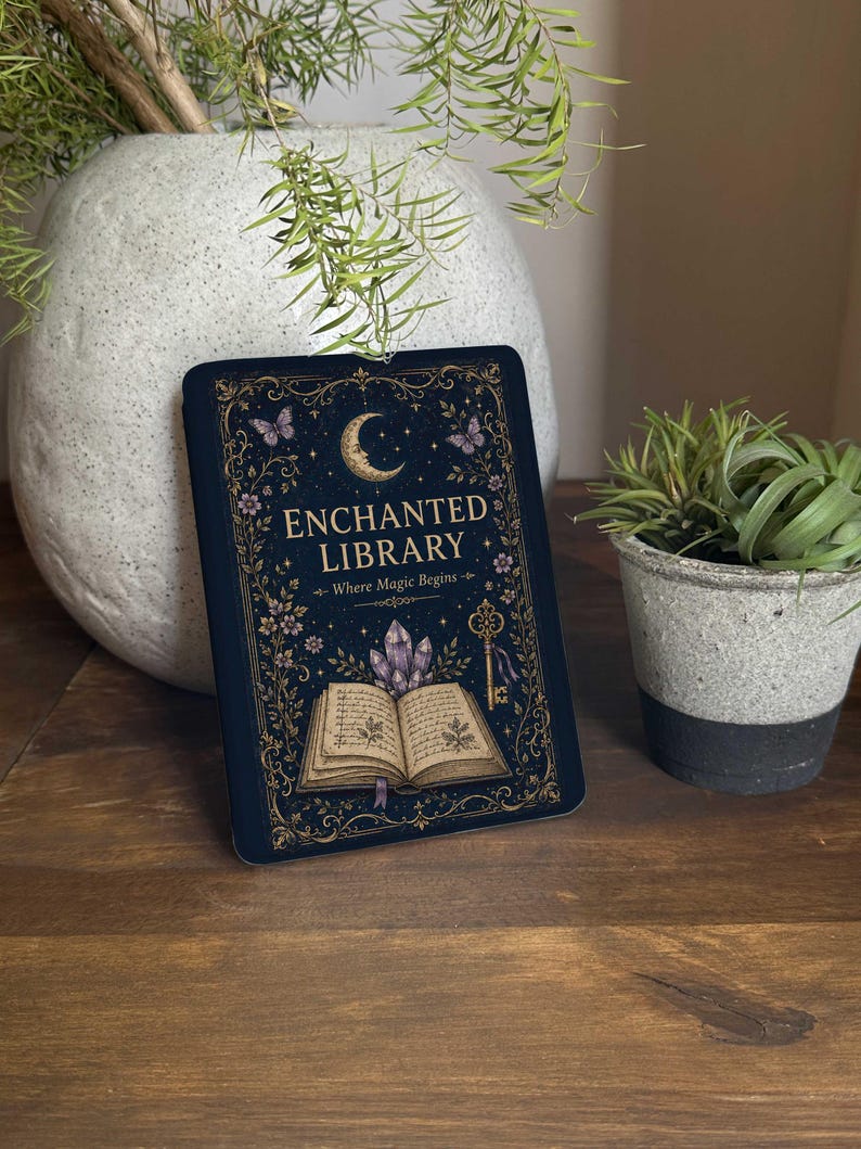May include: A rectangular sign with a dark blue background featuring gold filigree borders, a crescent moon, butterflies, a key, purple crystals, and an open book. The text reads ENCHANTED LIBRARY and Where Magic Begins in gold lettering.