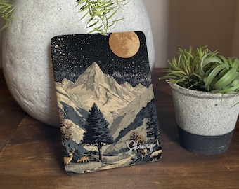May include: A rectangular notebook with a mountain landscape design. The cover features a starry night sky, a full moon, and a mountain range. The word "Sherry" is written in cursive. The notebook is displayed on a wooden surface.