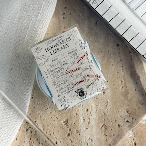 May include: A clear phone case featuring a printed Hogwarts Library checkout card design. The card includes columns for Name and Date due, with handwritten signatures like Remus Lupin and James Potter, and red stamped text reading OVERDUE.