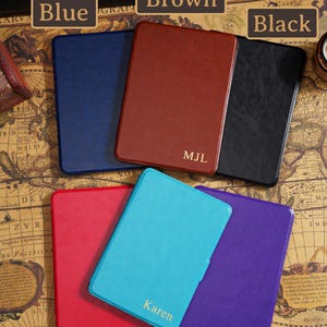 May include: A collection of leather-bound notebooks in various colors: blue, brown, black, red, light blue, and purple. The brown notebook is personalized with the initials "MJL", and the light blue notebook has the name "Karen".