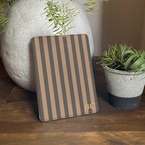 May include: A rectangular case with vertical brown and tan stripes. The case has gold-colored initials "BC" in the bottom right corner. The case is resting on a wooden surface.