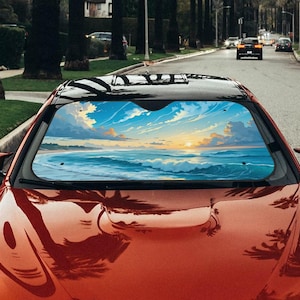 May include: A red car with a black roof and a windshield sunshade featuring a beach scene with blue waves, a sunset, and a cloudy sky. The car is parked on a tree-lined street.