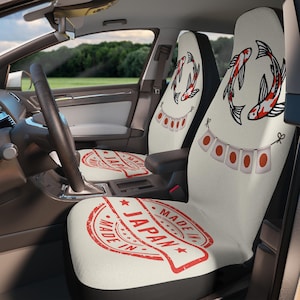 Puede incluir: Fundas para asientos de coche con temática japonesa. Las fundas presentan un sello rojo que dice "Made in Japan" y un diseño de dos peces koi. Los reposacabezas tienen una guirnalda de banderas rojas y blancas.